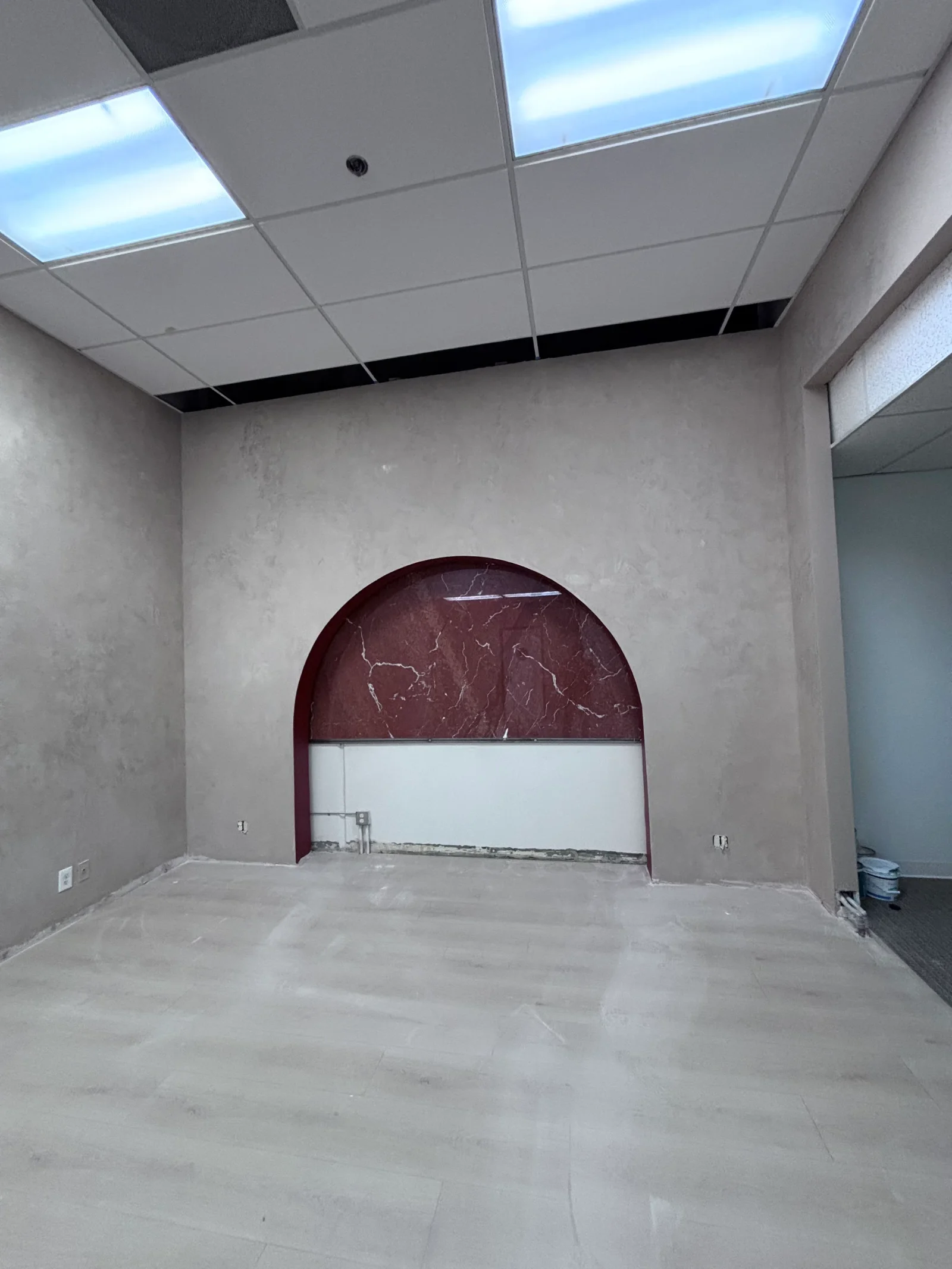 Commercial interior with concrete floor, gray walls, and burgundy marble arched accent wall with white panel insert