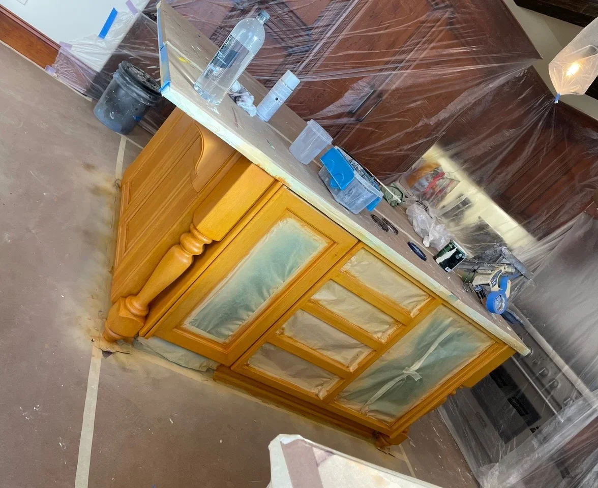 Golden wood cabinet with glass panels and turned spindle details during refinishing preparation