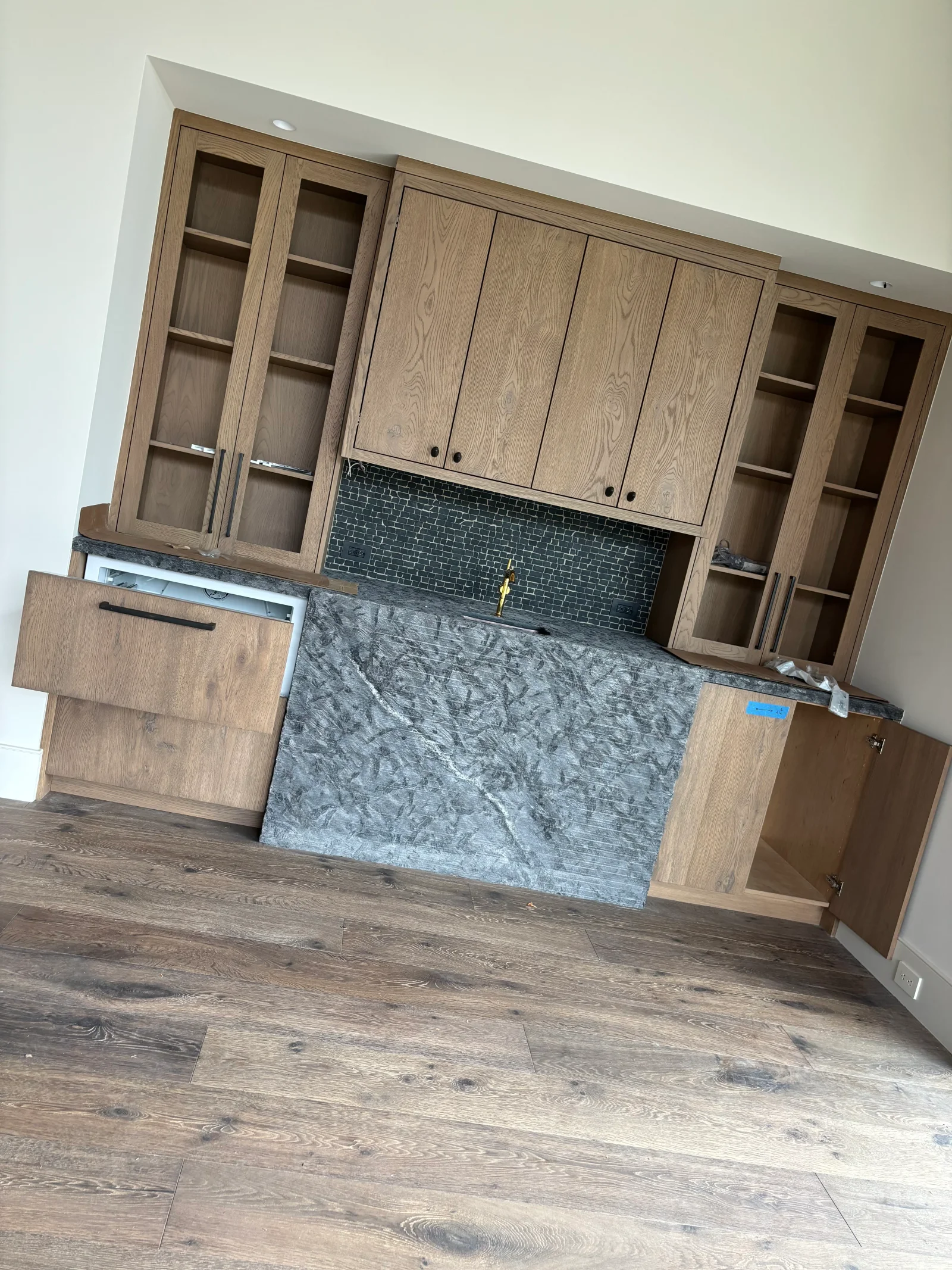 Oak kitchen cabinets with glass doors, quartz countertop, and dark subway tile backsplash