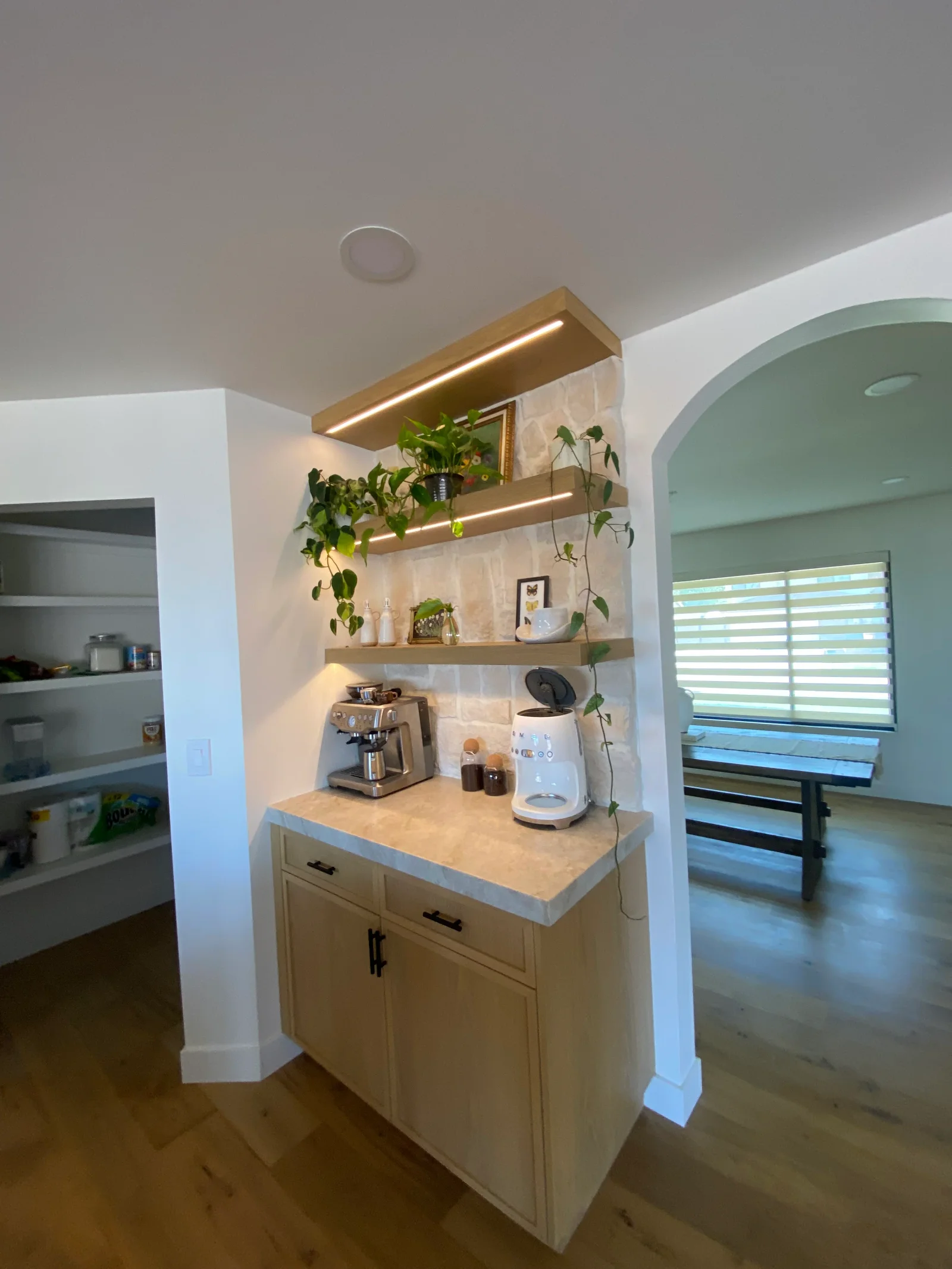 White painted kitchen beverage station with brass shelves, LED lighting, quartz counter, and sage green accent wall