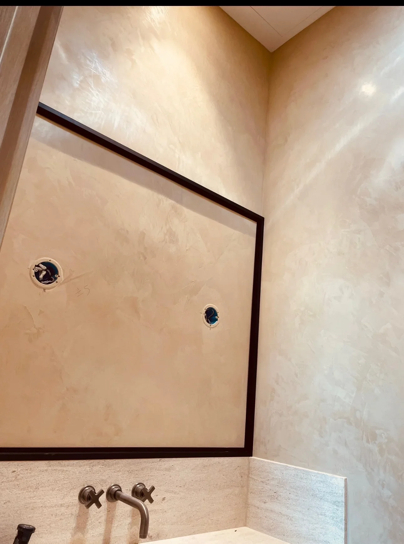 Polished plaster bathroom walls with dark-framed mirror and bronze fixtures