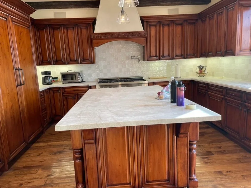 Cherry wood kitchen cabinets with marble island countertop and decorative backsplash