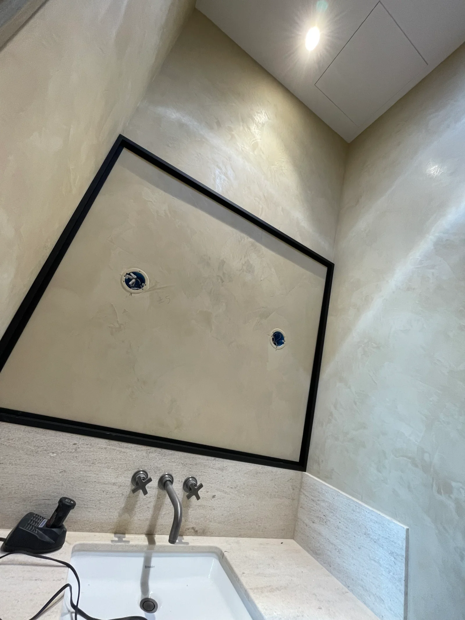Finished drywall bathroom with smooth compound walls, black-framed mirror, and wall-mounted faucet fixtures
